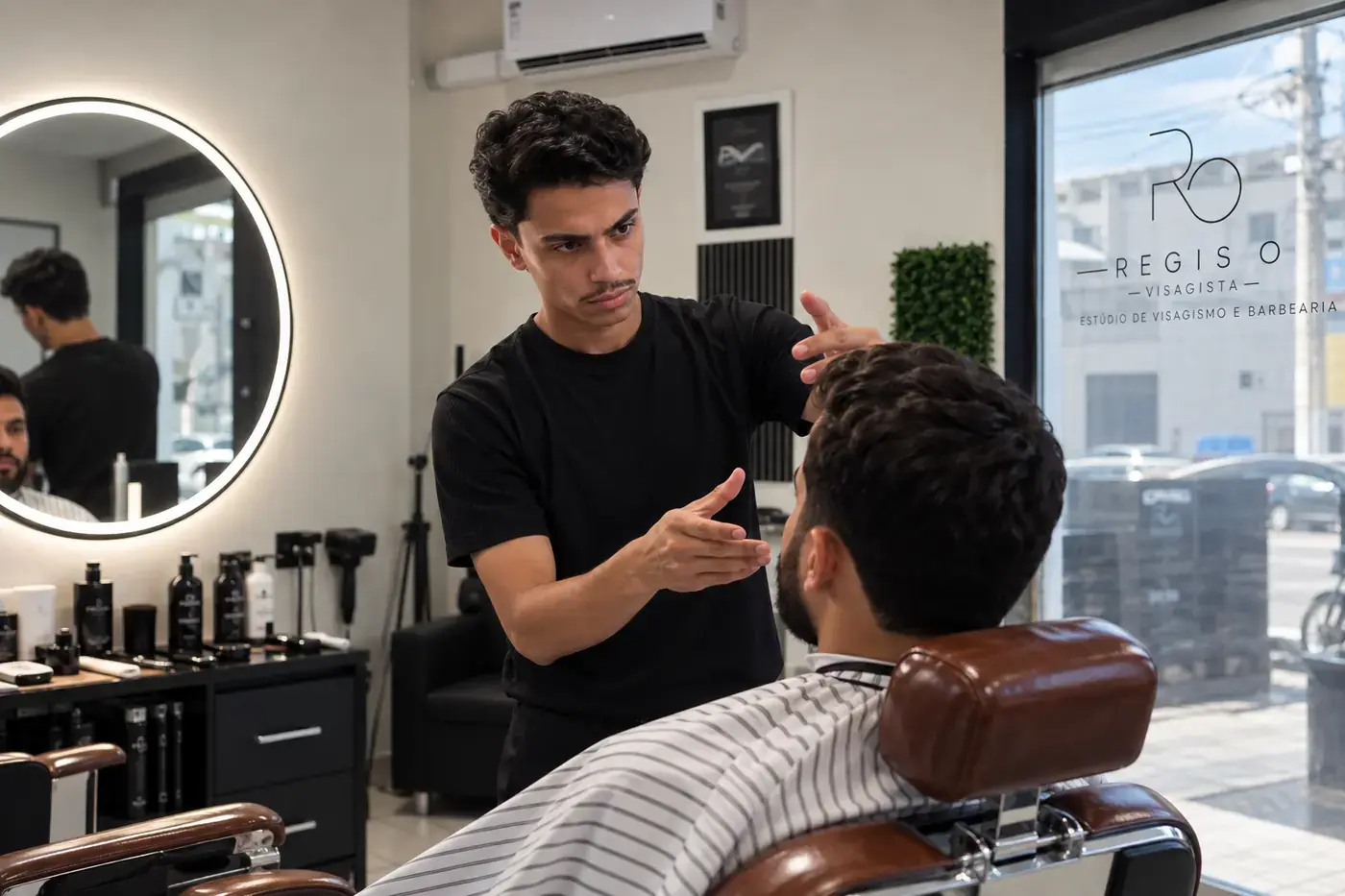 Regis conversa com o cliente na cadeira e explica, com as mãos, a direção do corte